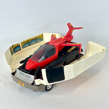 A vintage red and black toy vehicle model displayed inside an open cream-colored plastic display base on a light gray background.