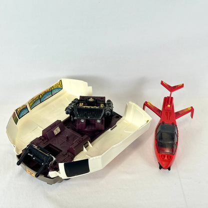 A vintage toy set featuring a red helicopter and a beige and dark purple vehicle inside its open cream-colored shell.