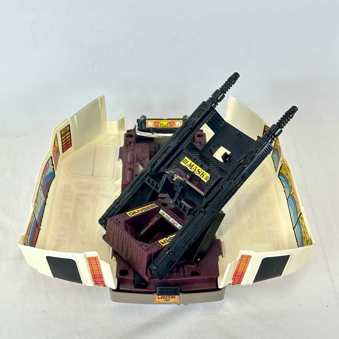 A vintage toy vehicle set featuring a black and dark purple gun turret mounted on a cream-colored plastic shell. 