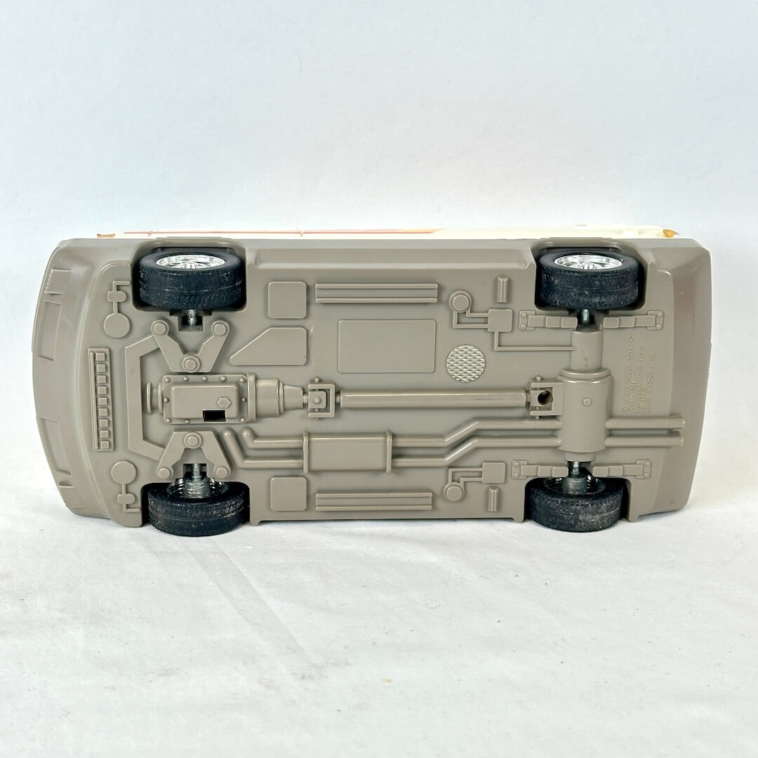 A toy model car shown from underneath, revealing a detailed suspension and chassis structure in a light gray plastic.