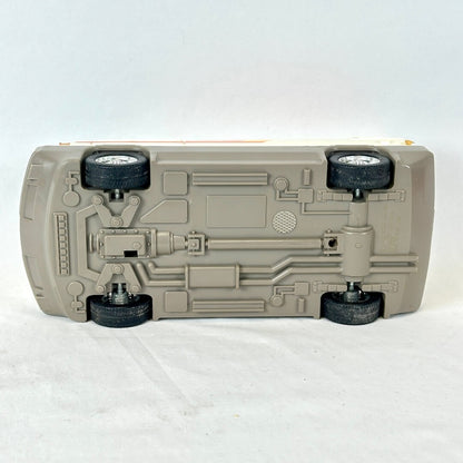 A toy model car shown from underneath, revealing a detailed suspension and chassis structure in a light gray plastic.