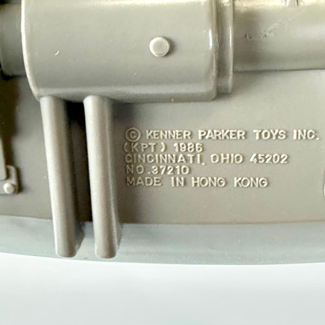 Close-up of a molded plastic toy part in a light gray color, featuring embossed text. 