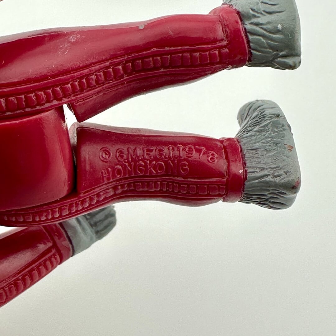 Close-up of red plastic toy figure with gray feet on a white background