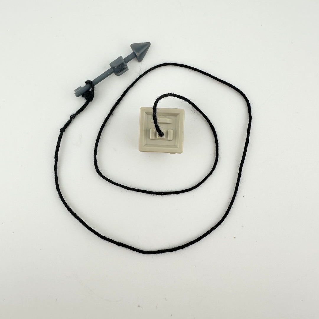 small beige cube with black string attached to tiny gray harpoon. 