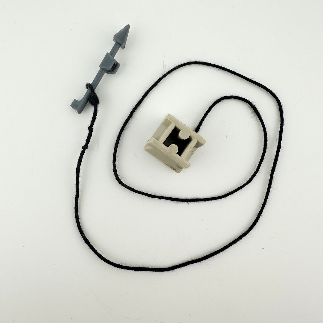 small beige cube with black string attached to tiny gray harpoon. 