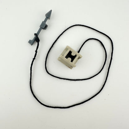 small beige cube with black string attached to tiny gray harpoon. 