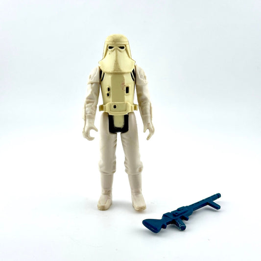 Toy figure of a character in a beige suit with a helmet, holding a blue weapon on a white background