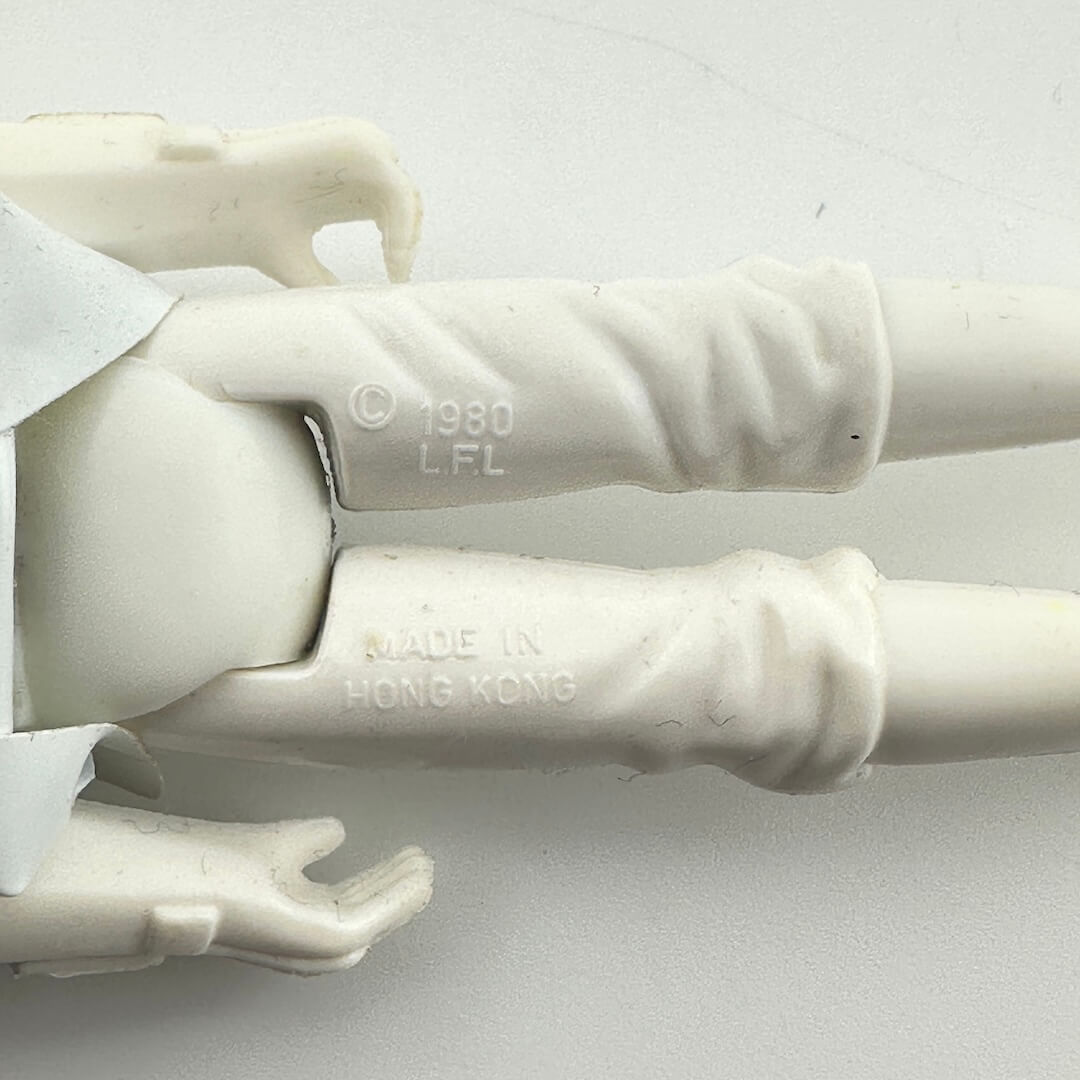 Close-up of a white plastic action figure's lower legs and hands, showing embossed text '© 1980 L.F.L'