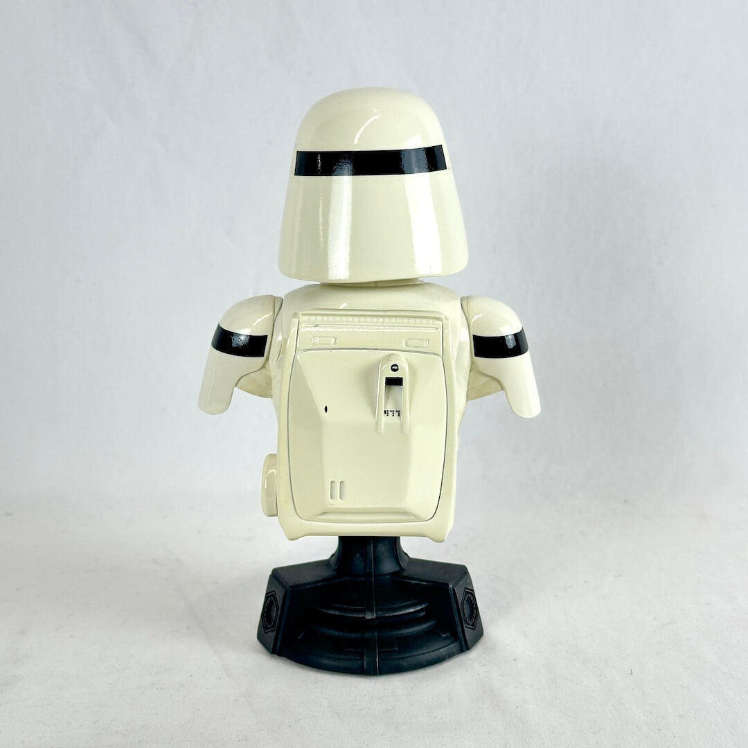 A retro-style white and black toy robot figure standing on a black base against a light gray background.