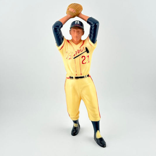 Figurine of baseball player in Braves uniform in mid-wind up to pitch, so arms raised with hands & glove over head.
