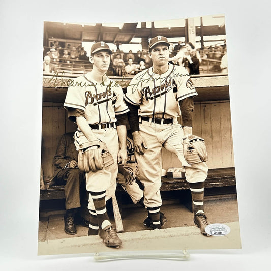 Two baseball players in vintage uniforms sitting in a dugout with signatures on the photo.