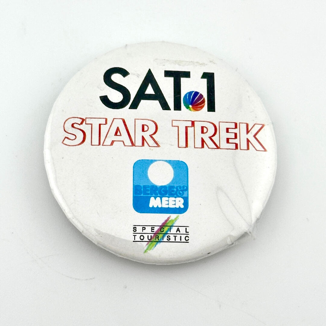 White circular pin with text and "Star Trek" branding. 
