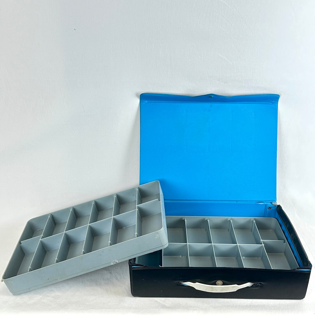 Interior contents of carrying case including two gray trays with dividers inside blue and black case. 