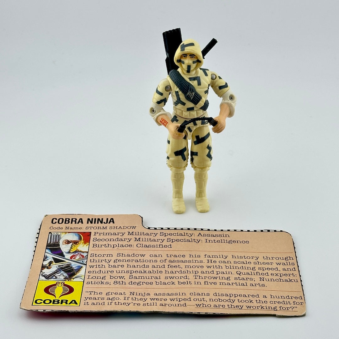 White male action figure in white camo with black details, pictured with accessories and cardboard ID card.