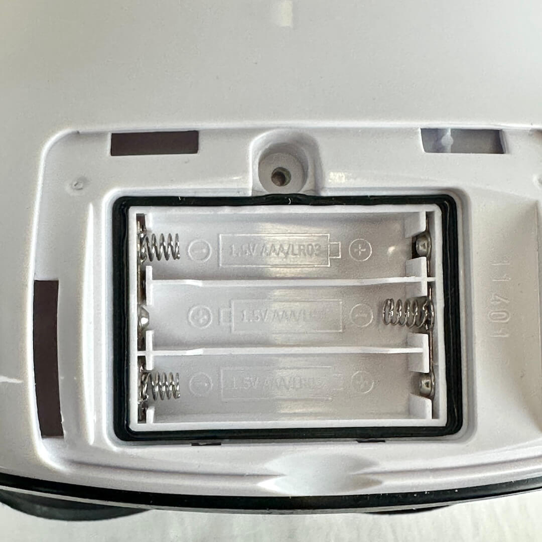 Close-up of a white helmet's battery compartment for three 1.5V AAA/LR04 batteries inside a black-rimmed slot with metal springs.