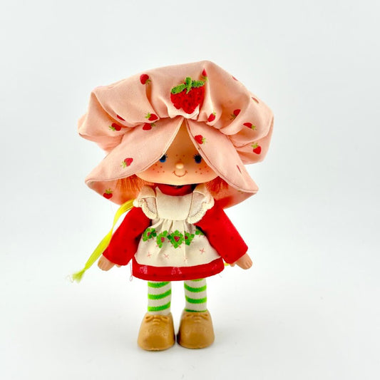 Toy doll with pink hat and red dress against white background. 