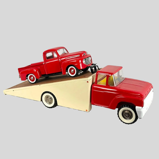 Red toy truck with a smaller red truck on a wooden flatbed trailer against a light gray background