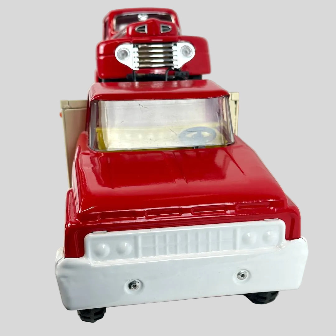 Red toy truck with red toy truck on trailer against gray background. 