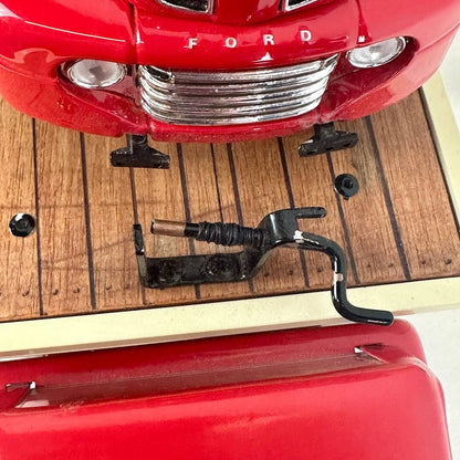 Close-up of a red Ford vehicle's grille and front bumper on a wooden surface.