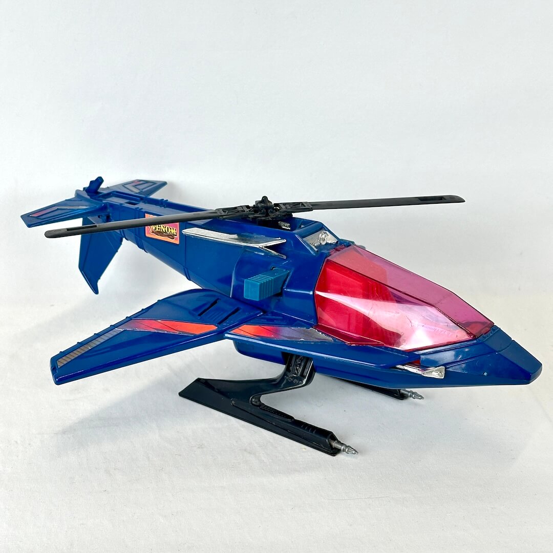 A blue toy jet aircraft model with a red translucent nose section, black rotor blades and landing gear.