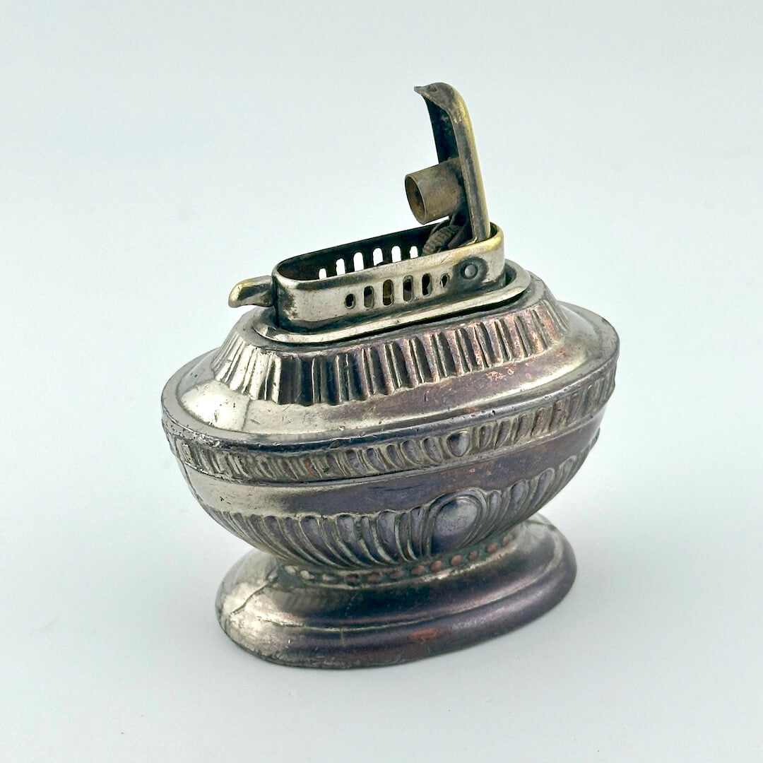 An antique silver-toned lighter with a decorative ribbed body and a hinged lighter mechanism on top.