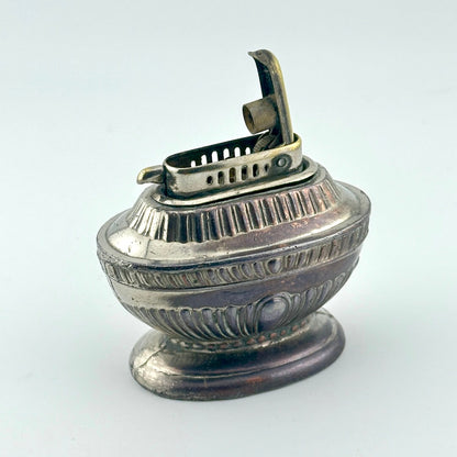 An antique silver-toned lighter with a decorative ribbed body and a hinged lighter mechanism on top.
