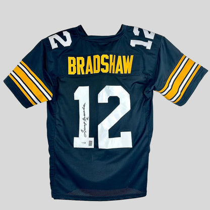 A black football jersey with gold accents on sleeves, nameplate reading "Bradshaw," number '12' with signature on the 1. 