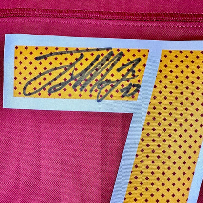 A close-up of a red textured fabric, featuring a white-bordered patch with a yellow background, and signature. 