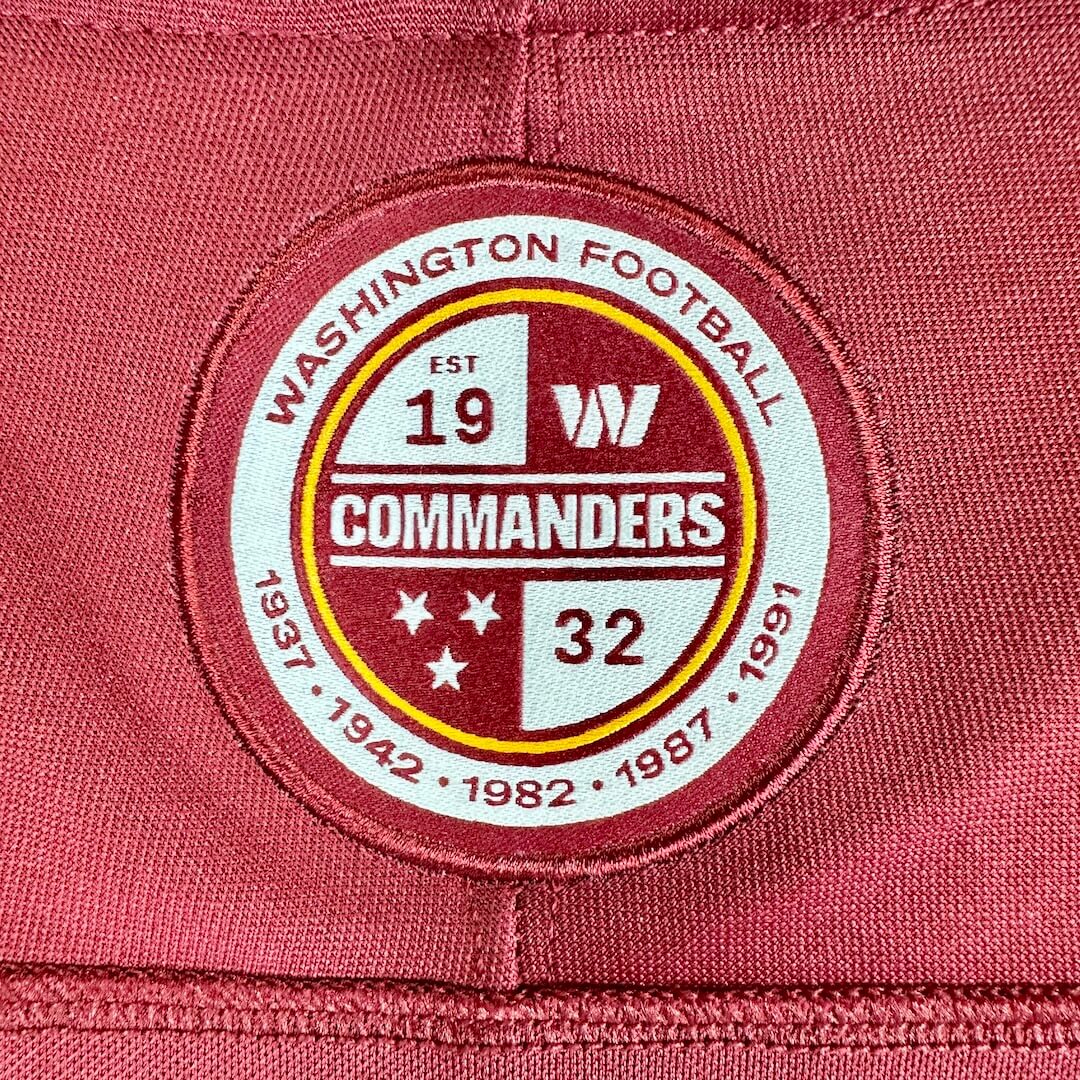 A close-up of a circular embroidered patch on a maroon red fabric background. 