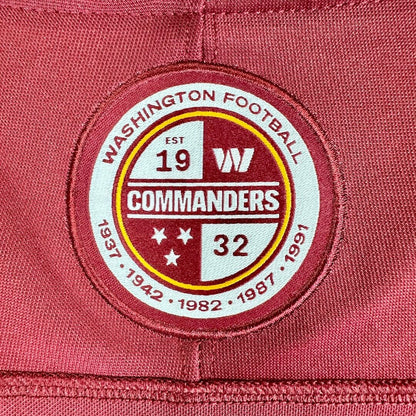 A close-up of a circular embroidered patch on a maroon red fabric background. 