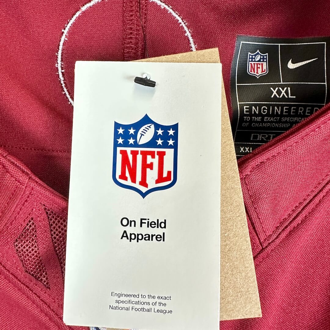 A close-up of a football jersey showing the NFL shield logo on a white hangtag and a black Nike tag indicating XXL size.