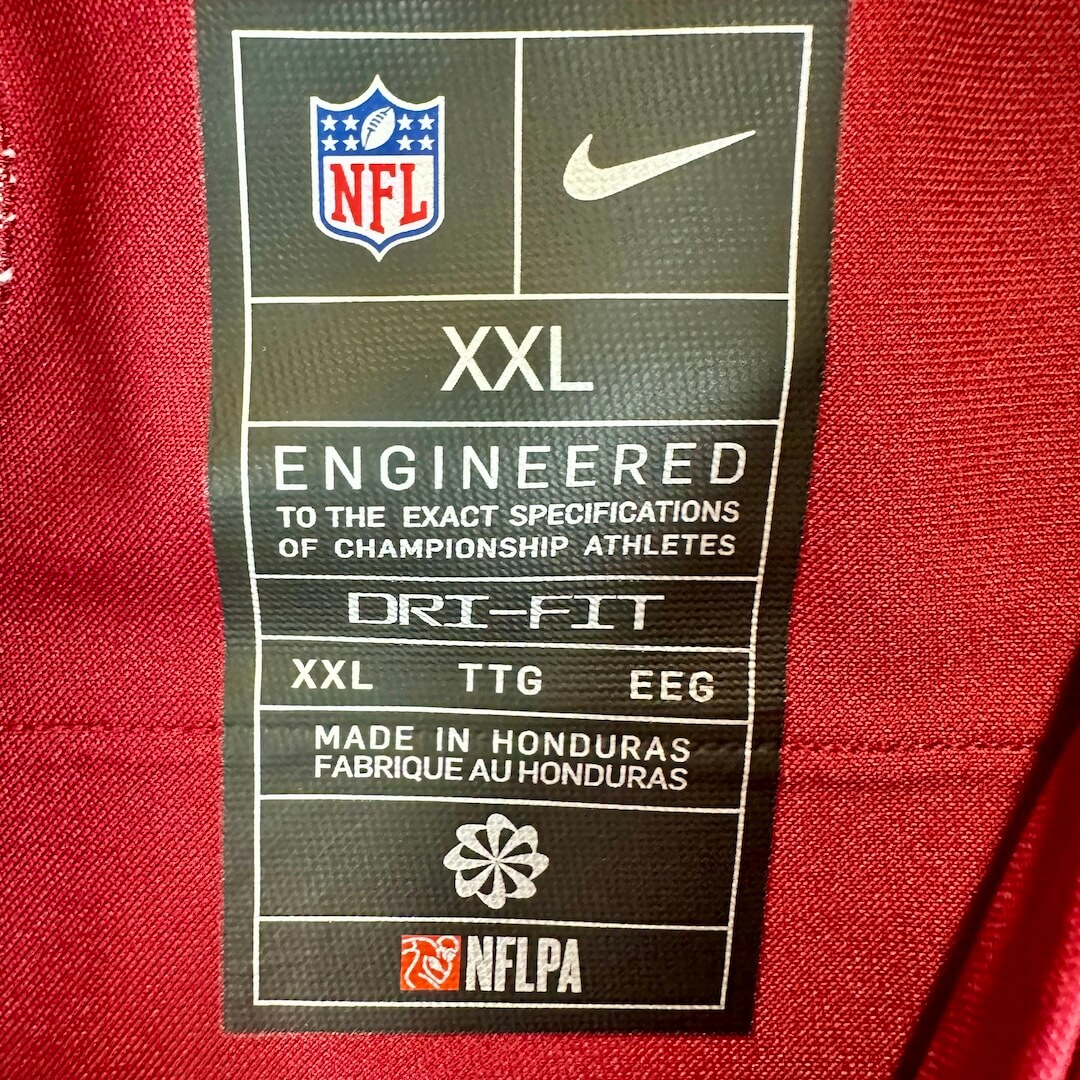 Close-up of a black NFL and Nike garment care label sewn onto a red athletic jersey.