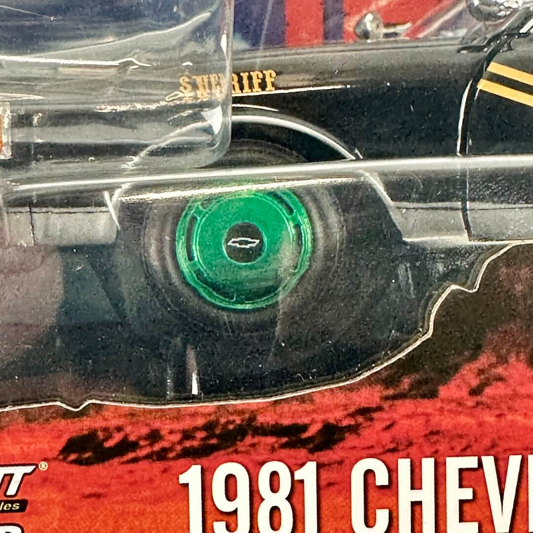 Close-up of a packaged diecast car, and a bright green wheel in center, inside clear plastic blister packaging.