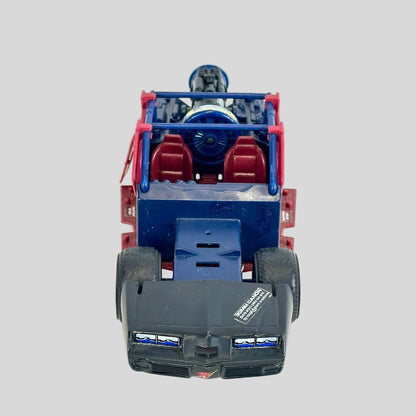 A toy vehicle front. The vehicle features a dark blue body, red roll cage and seats, and a black front bumper and wheels.