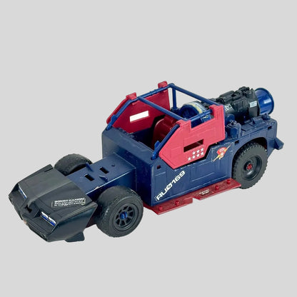 A vintage toy vehicle, featuring a blue chassis with red roll cage and side panels, black wheels, and a black front bumper.