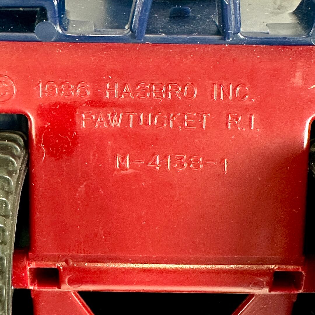 Close-up of the underside of a red plastic toy vehicle, showing embossed text that reads '1986 HASBRO INC. PAWTUCKET R.