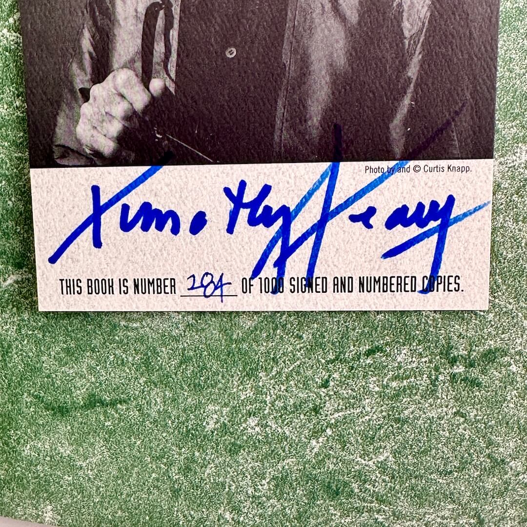 Close-up of a signature on a book with a black and white photo above it, on a textured green background.