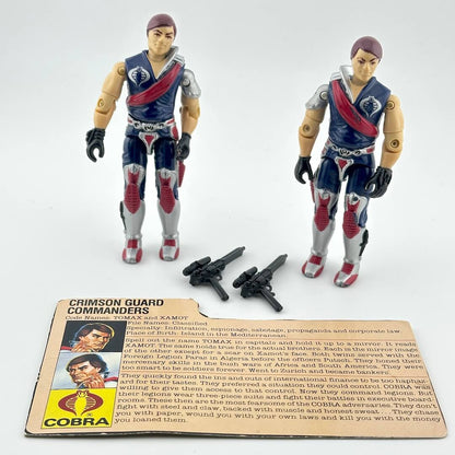 Two action figures with accessories and character card against white background. 