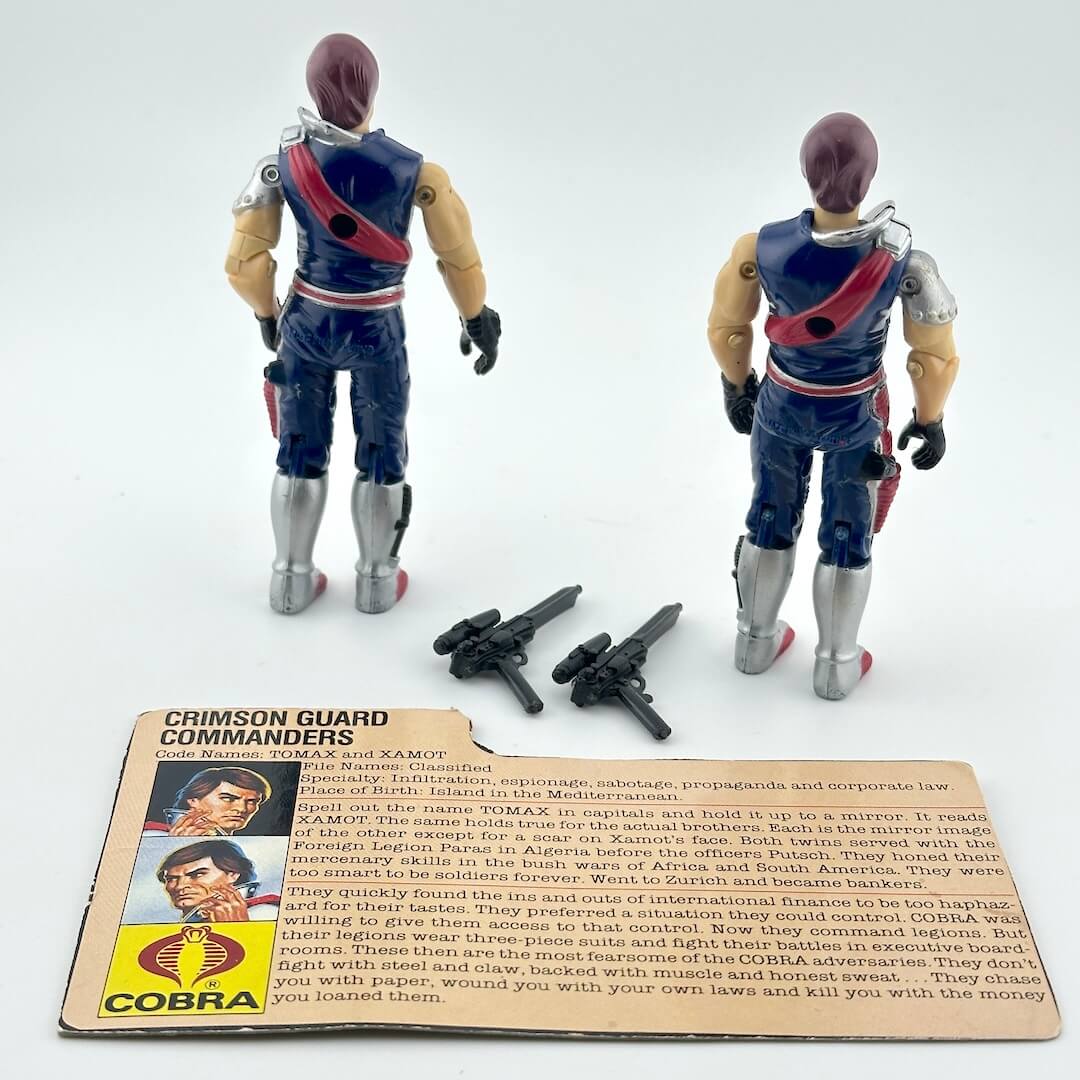 Two action figures with accessories and character card against white background. 