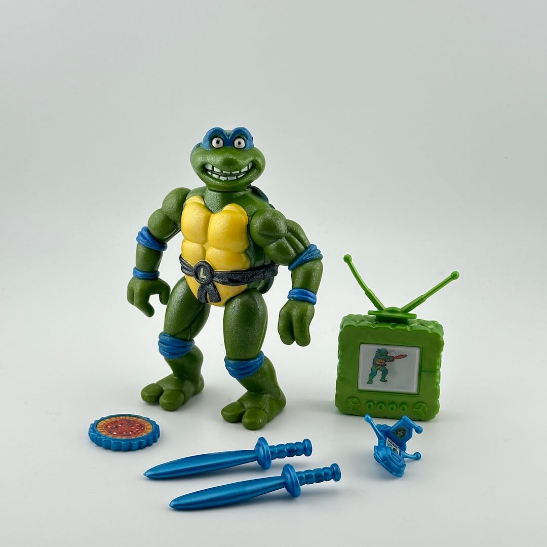 Anthropomorphized turtle with glittery skin & poppin eyes pictured with blue accessories & green TV.