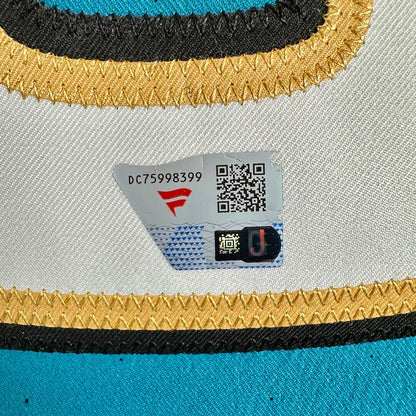 Close-up of a jersey with black and gold striped trim, showing a authentication tag with a QR code, barcode, and red logo.