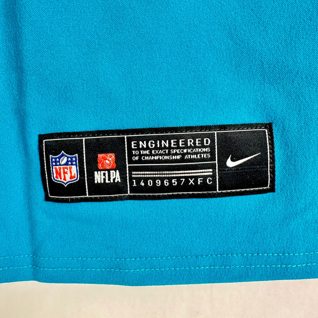 Close-up of a bright turquoise Nike NFL jersey showing the black and white NFLPA tag with NFL and Nike logos.