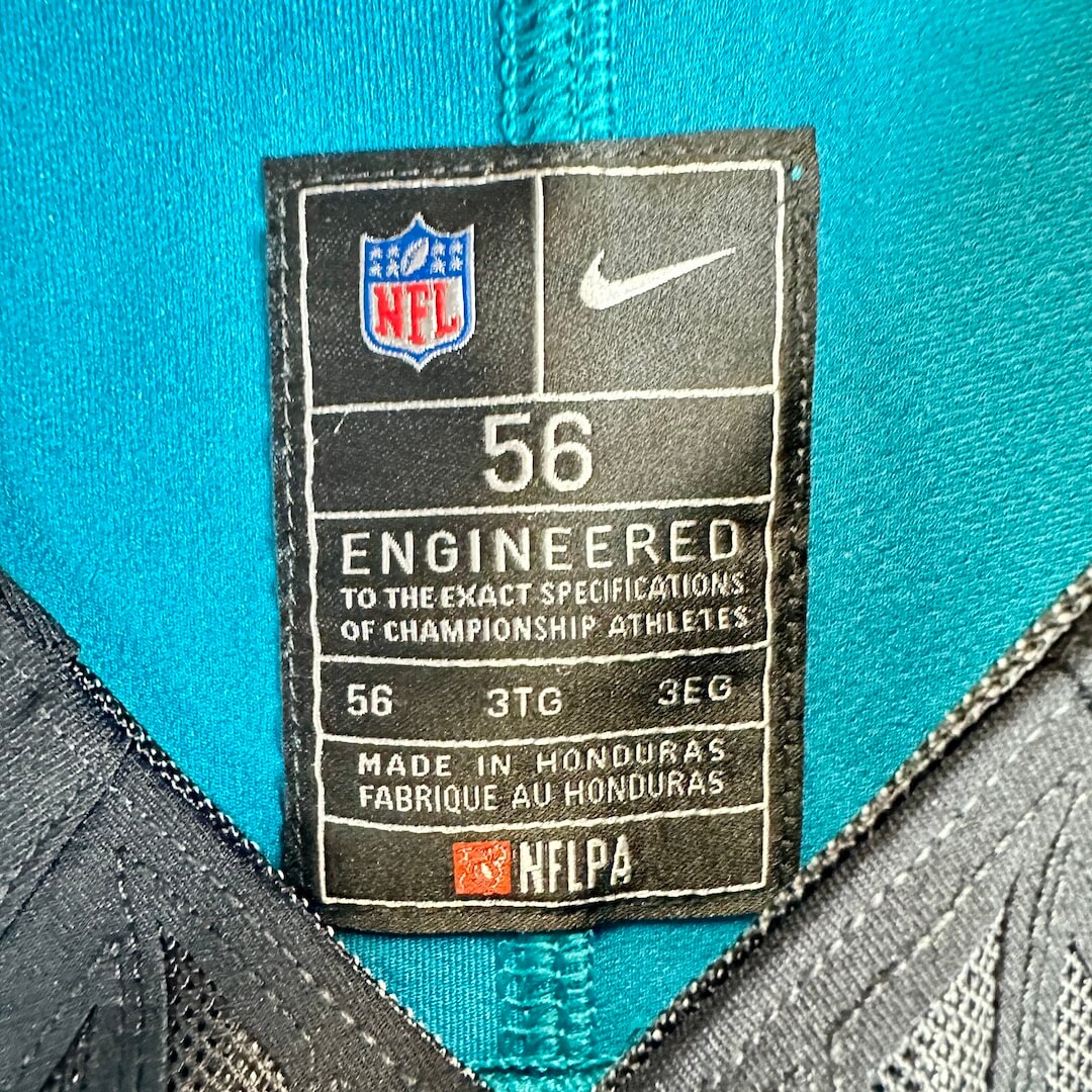 Close-up of an NFL and Nike size tag on a teal football jersey, showing size 56 and manufacturing details.