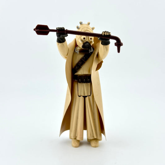 Toy figure of a character in tan robe holding a staff on a white background