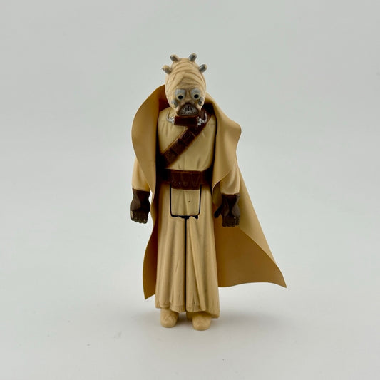 Action figure in all tan, wearing tan cape, brown gloves, brown belt, and tan wrapped face with mouthpiece.