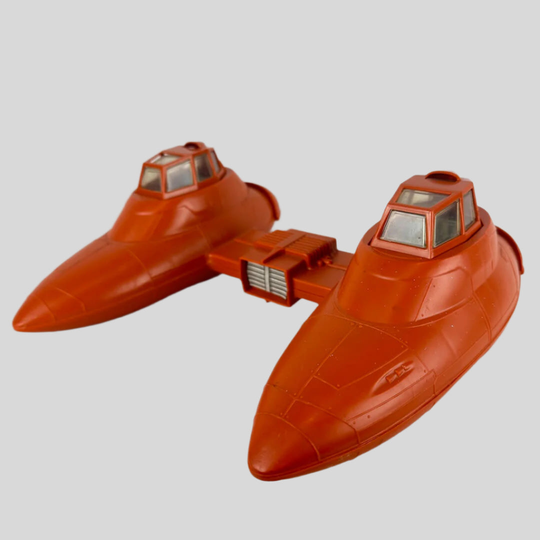 Orange toy spaceship with two compartments attached between them against gray background.
