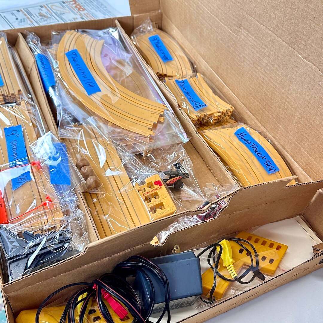 Box containing toy tracks and accessories with clear plastic packaging.