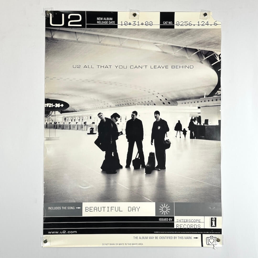 black and white promo poster for U2 album release with image of band in airport at center, text at top & bottom