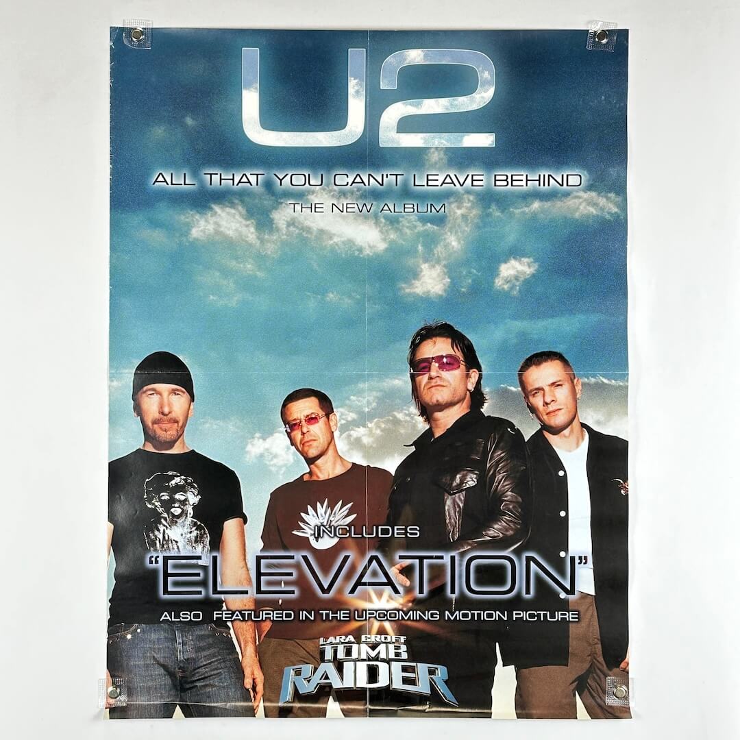 Promotional poster for U2's album 'All That You Can't Leave Behind' featuring four band members against a cloudy sky.
