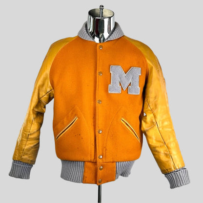 Orange jacket with lighter orange sleeves. Cuffs, collar & waistband all ribbed grey. "M" on breast in grey.